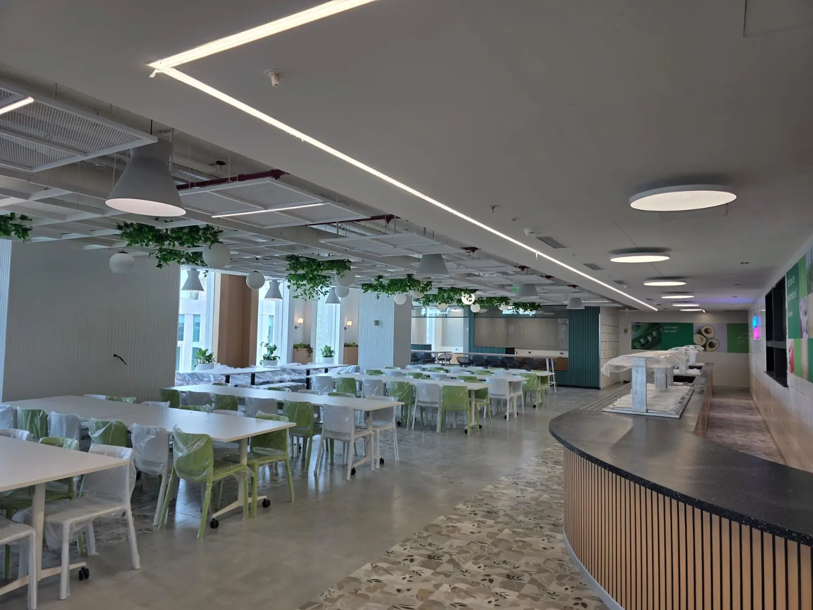 Corporate cafeteria with recessed linear light lines, round surface luminaires and cone pendants