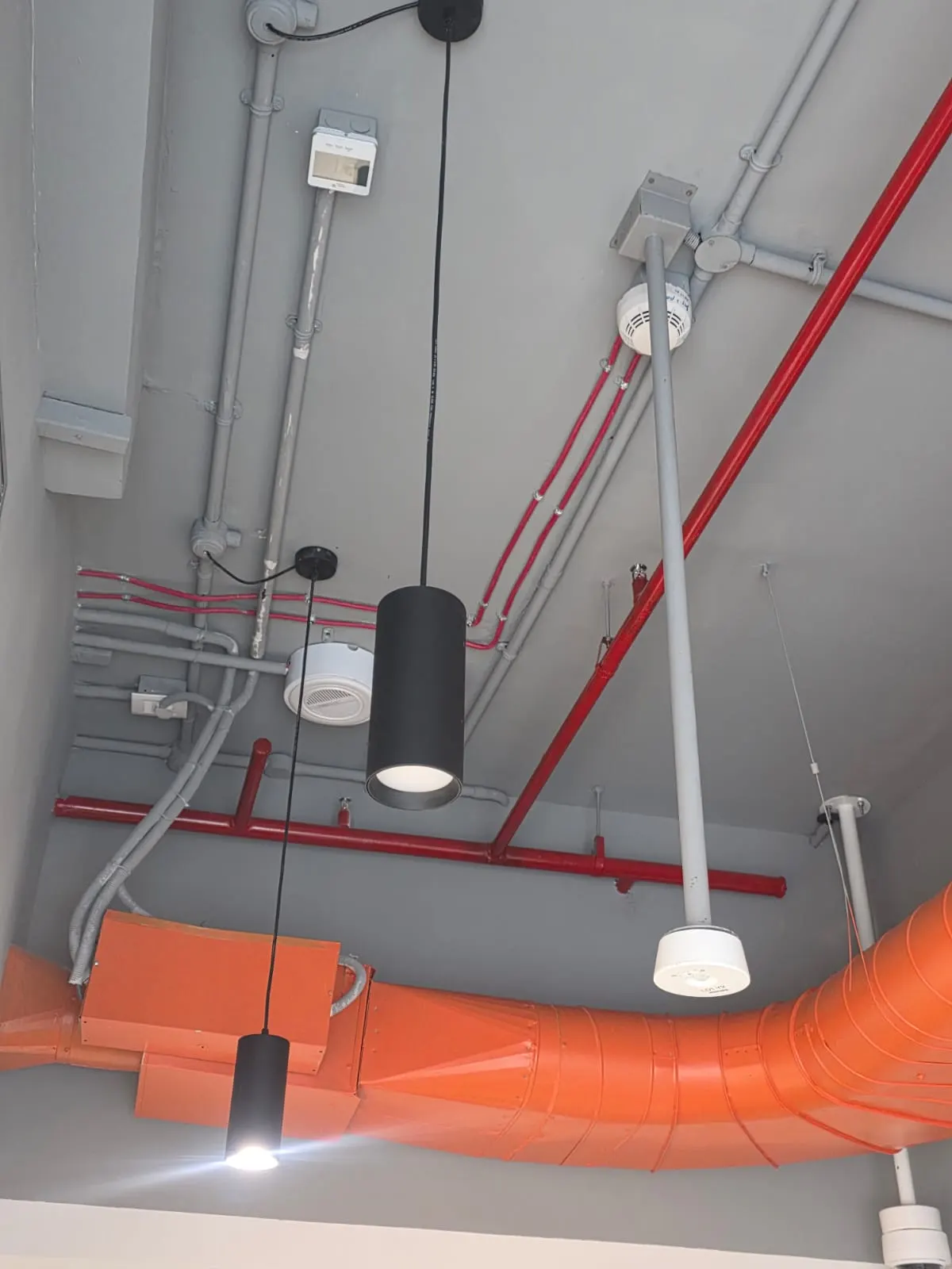 Two black cylinder pendants hanging at staggered heights under an exposed ceiling