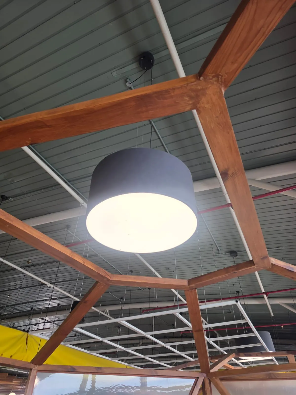 Large dark drum pendant hanging inside a timber hexagonal frame structure