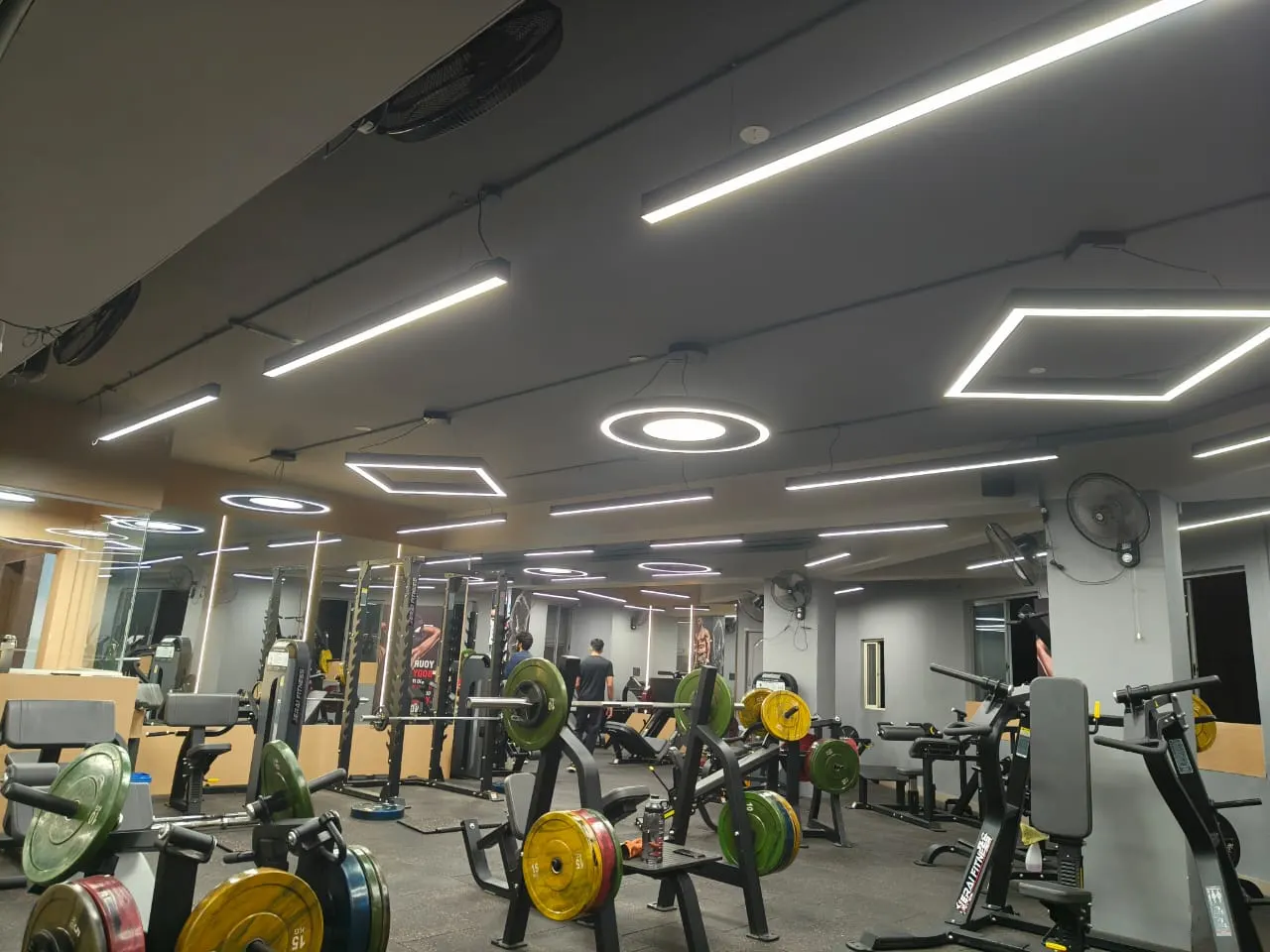 Fitness centre with suspended linear, ring and hexagon luminaires on a grey ceiling