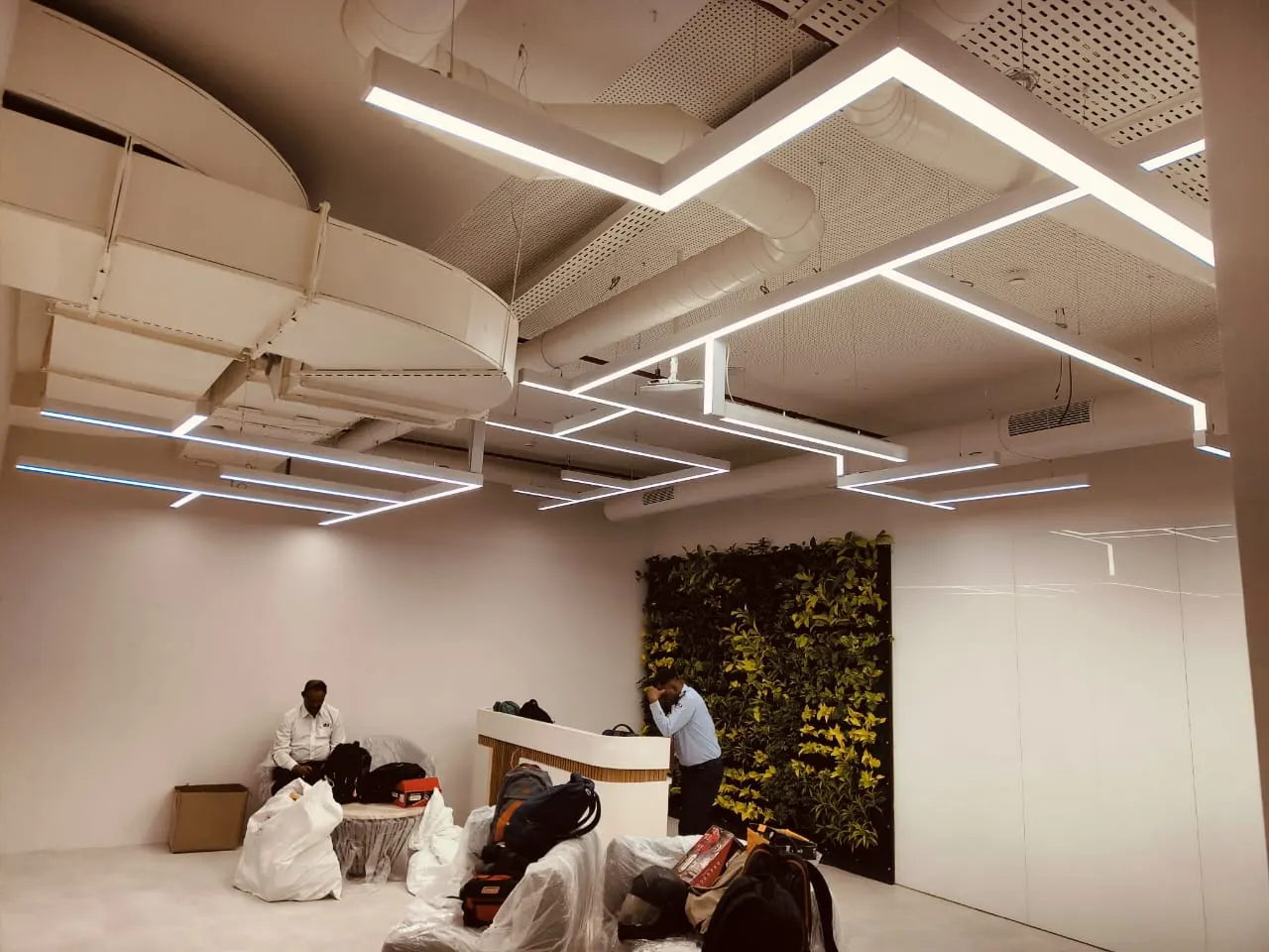 Reception area with suspended interlocking white linear profile luminaires beneath an exposed ceiling