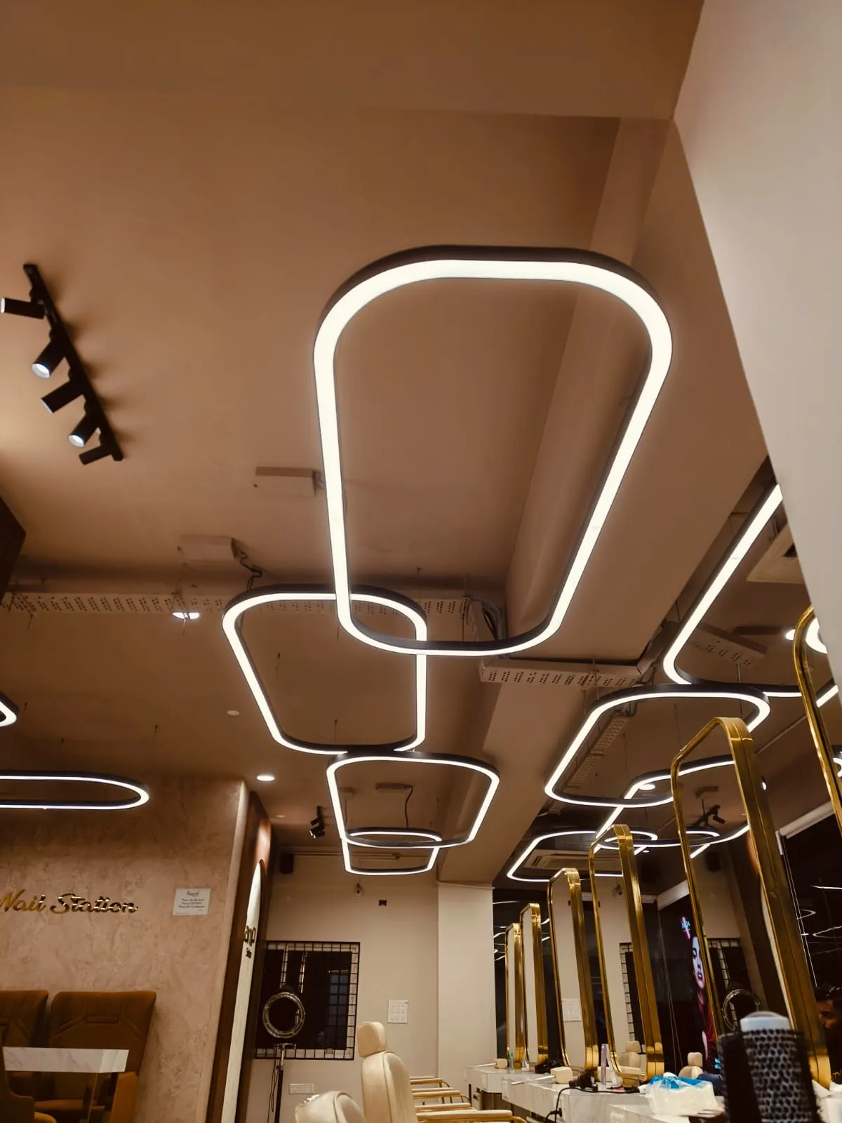 Salon ceiling with warm-white rounded-rectangle suspended profile luminaires and black track spotlights
