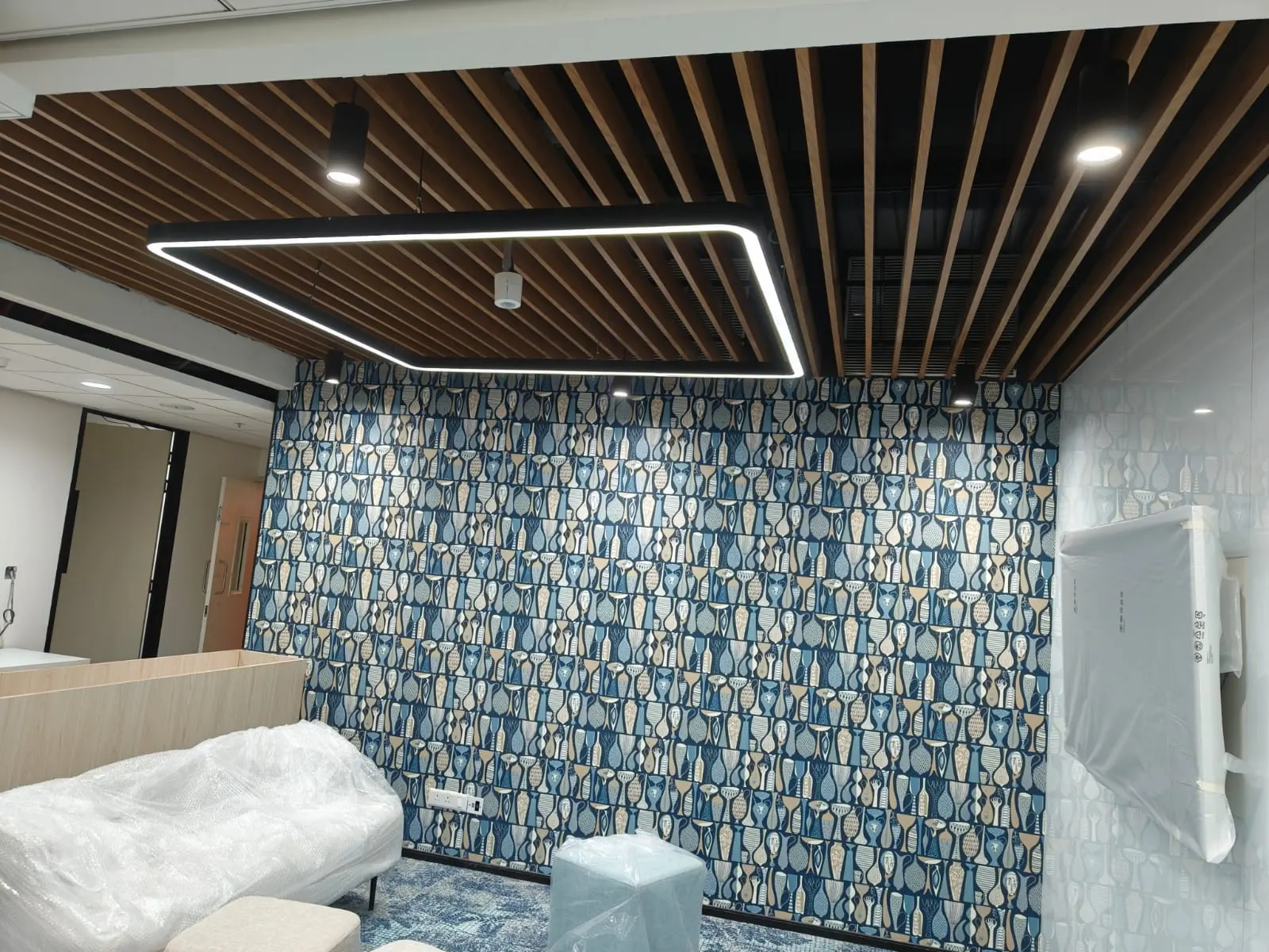 Black square profile pendant beneath a timber baffle ceiling in front of a patterned wall