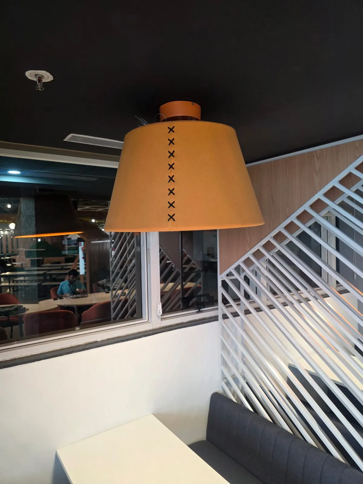 Tapered tan fabric pendant with black cross stitching over a dining booth